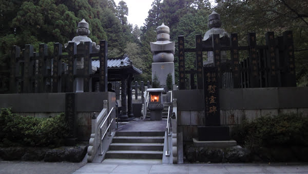 stairs lead to a raised section with a lit stone latern and several small buildings and stone markers